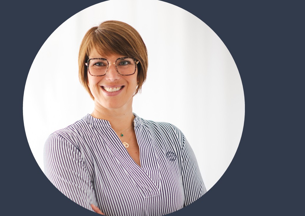 Professionelles Porträt einer Frau mit kurzen, braunen Haaren und Brille, die in einem gestreiften Oberteil lächelt. Der Hintergrund ist hell und unscharf, was den Fokus auf die Person lenkt.