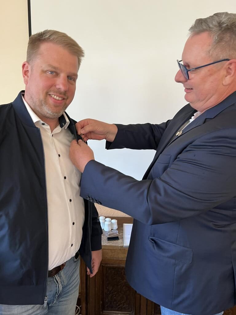 Zwei Männer bei feierlicher Ehrung, einer erhält eine Anstecknadel für langjähriges Engagement im Handwerk.