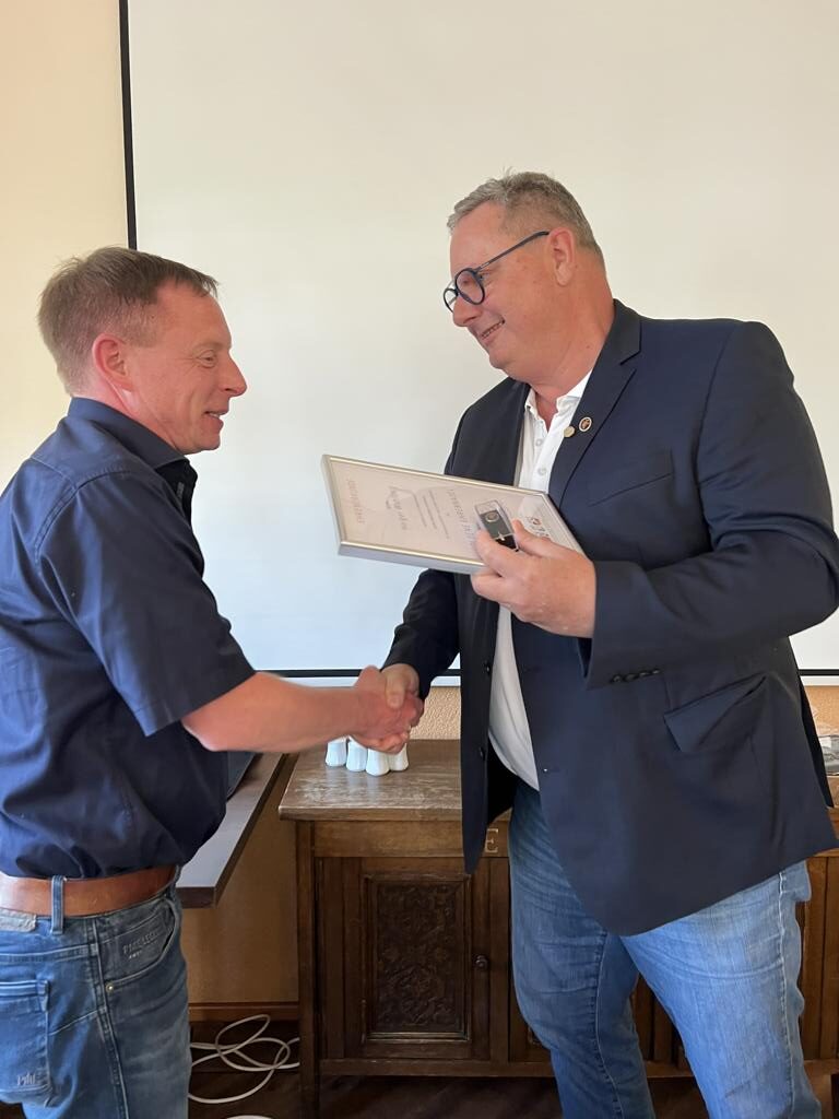 Zwei Männer bei feierlicher Übergabe einer Ehrenurkunde für langjähriges Engagement im Handwerk, Händedruck und Auszeichnung im Innenraum.