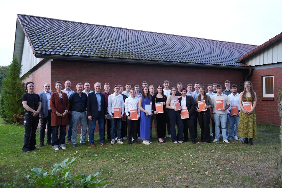Gruppenfoto von jungen Erwachsenen und Ausbildern bei einer Abschlussfeier vor einem Backsteingebäude, mehrere Personen halten Urkunden in der Hand