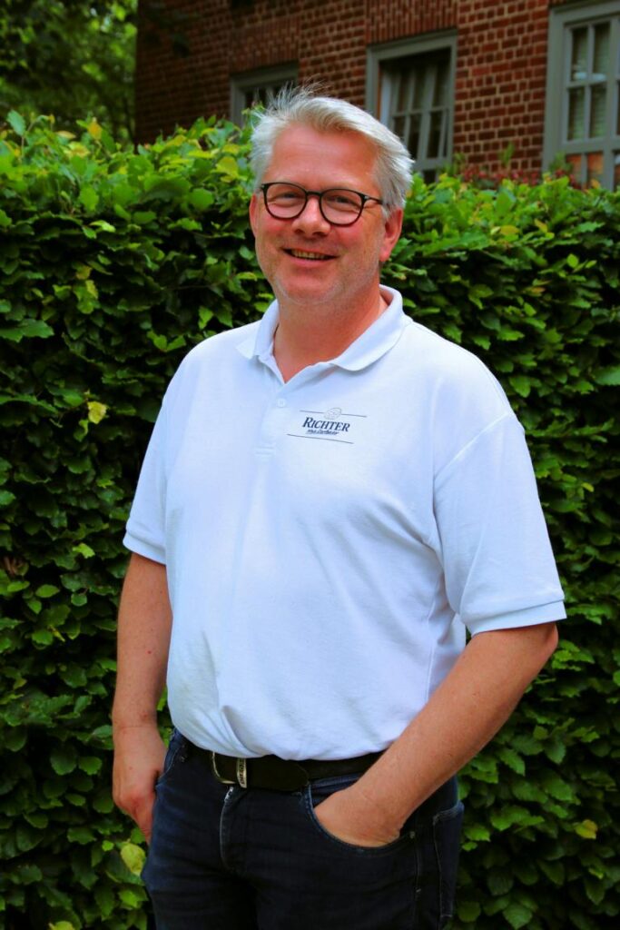 Mann mit Brille und weißem Polohemd vor grüner Hecke, repräsentiert Bäcker Stade für die Bäcker-Innung Harburg-Lüneburg-Stade